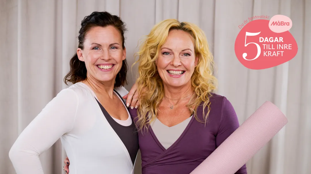 Två kvinnor som ler mot kameran. Ena kvinnan håller en yogamatta i handen.